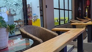 A seating area with wicker chairs and wooden tables, a glass table in the foreground, and a view of the street through large windows. - Jiahe Homestay (Emeishan Tourism Passenger Transport Center Baoguosi Station) (Emeishan City)