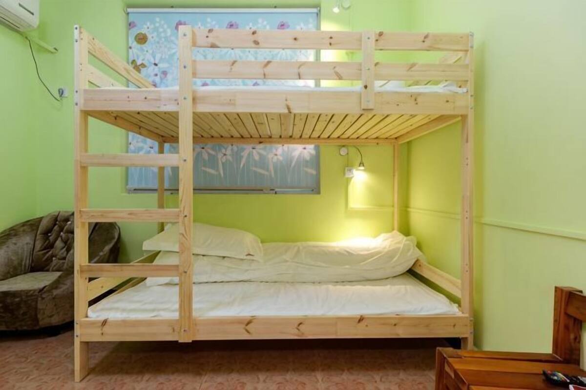 A bunk bed with a ladder, a single bed, a wall-mounted lamp, a window with a floral design, and a chair.