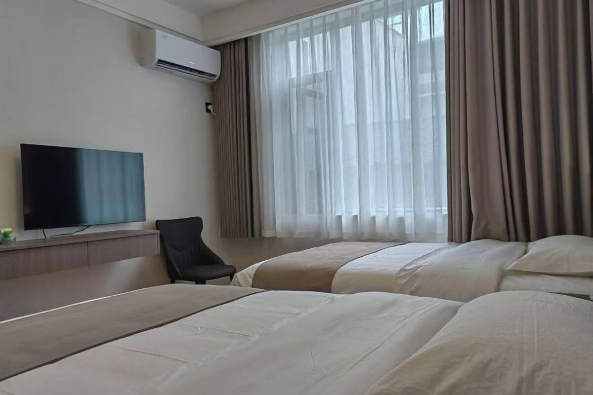 A hotel room with a flat-screen TV, a chair, and two beds with beige bedding.