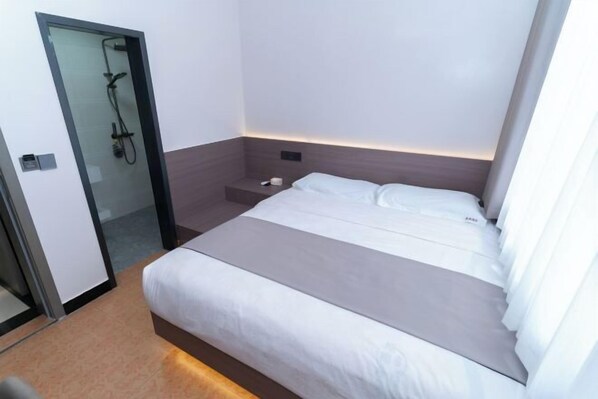 Une chambre d’hôtel moderne équipée d’un lit, d’une table de chevet, d’une petite table et d’un espace douche.