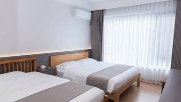 A hotel room with two beds, a wooden headboard, a nightstand, a desk, and a large window with sheer curtains.