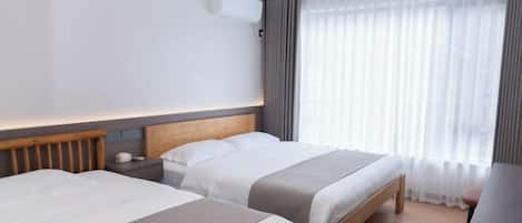 A hotel room with two beds, a wooden headboard, a nightstand, a desk, and a large window with sheer curtains.