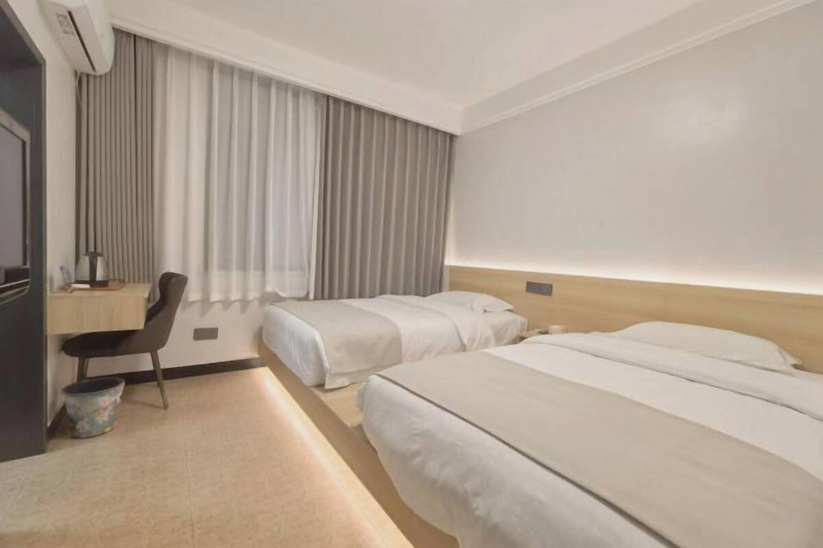 A hotel room with two beds, a desk, a chair, and a large window with curtains.