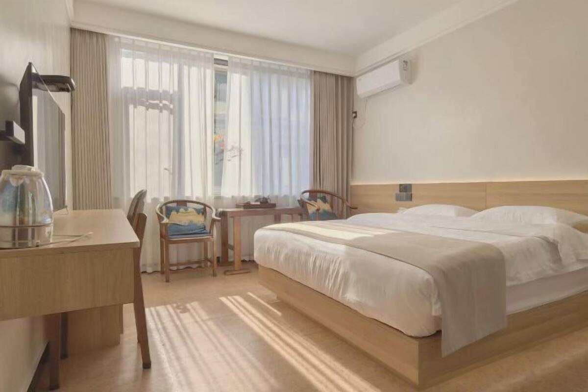A hotel room with a bed, a desk, a chair, and a window with curtains.