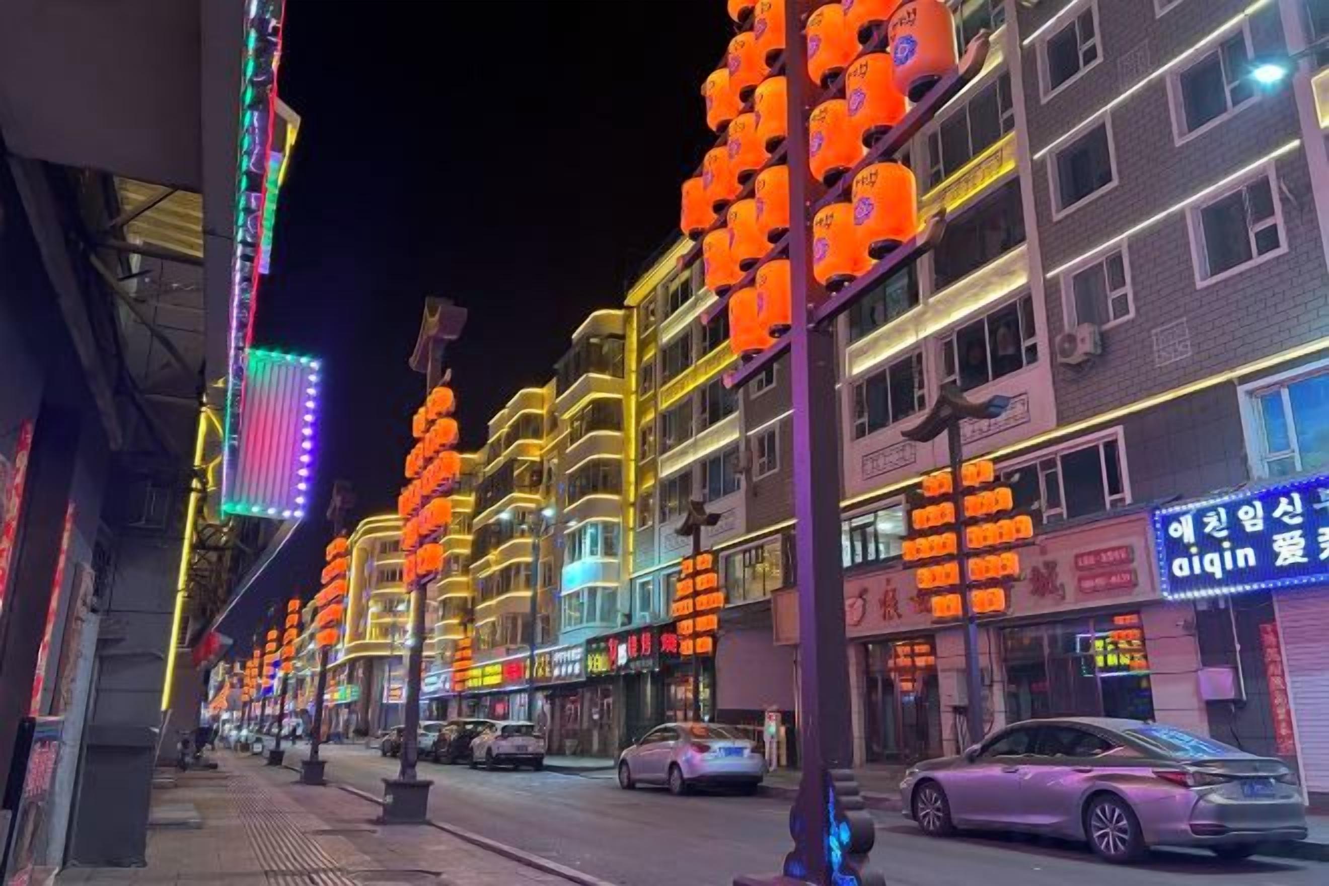 A street lined with brightly lit buildings and a car parked on the side.