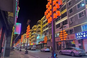 A street lined with brightly lit buildings and a car parked on the side.