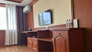 A hotel room with a wooden cabinet, a flat-screen TV mounted on the wall, a desk, and a chair. - Jiang Zhi Yuan Inn (Changbai County)