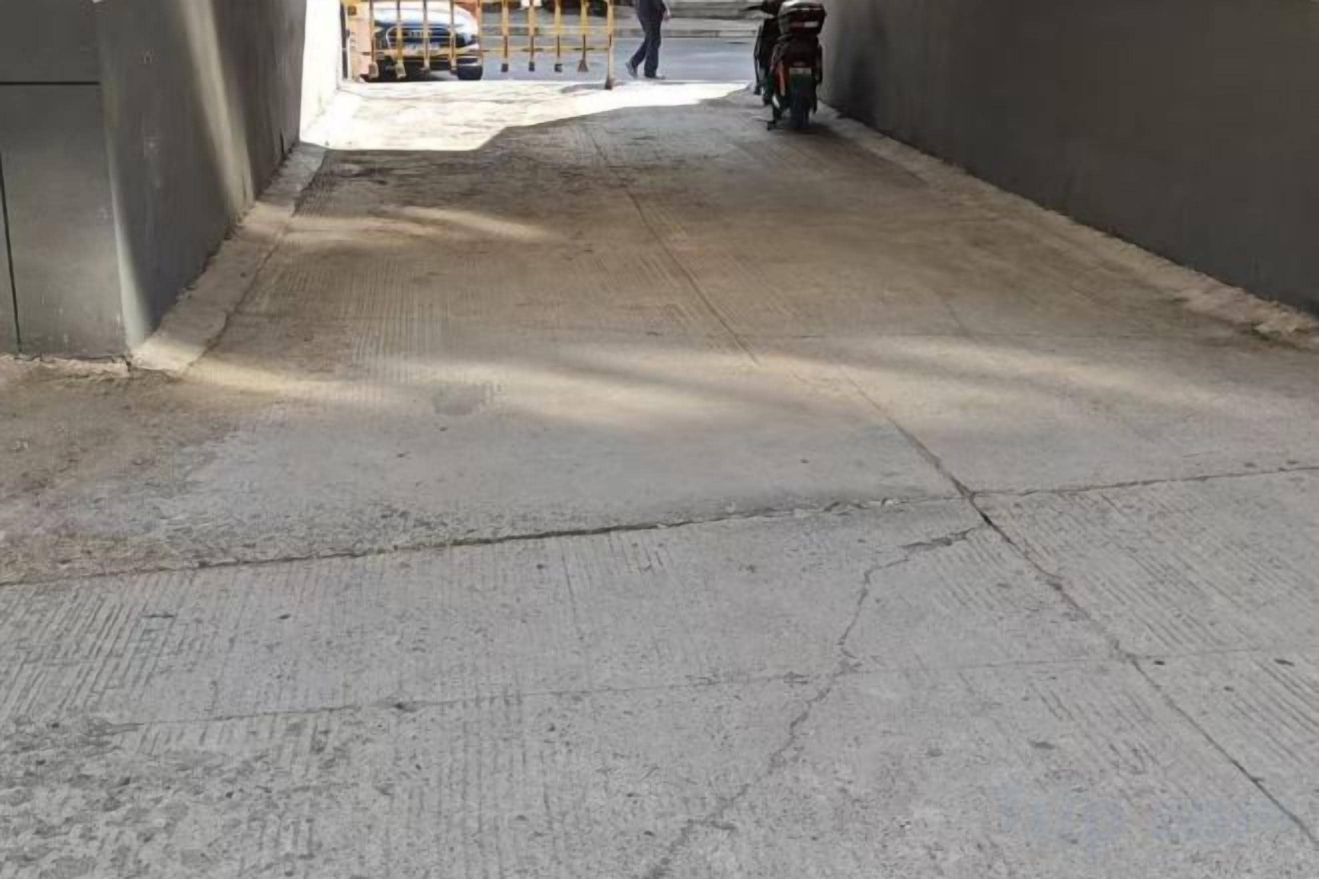 Un chemin en béton mène à un véhicule et à une moto, et on aperçoit une personne au loin.
