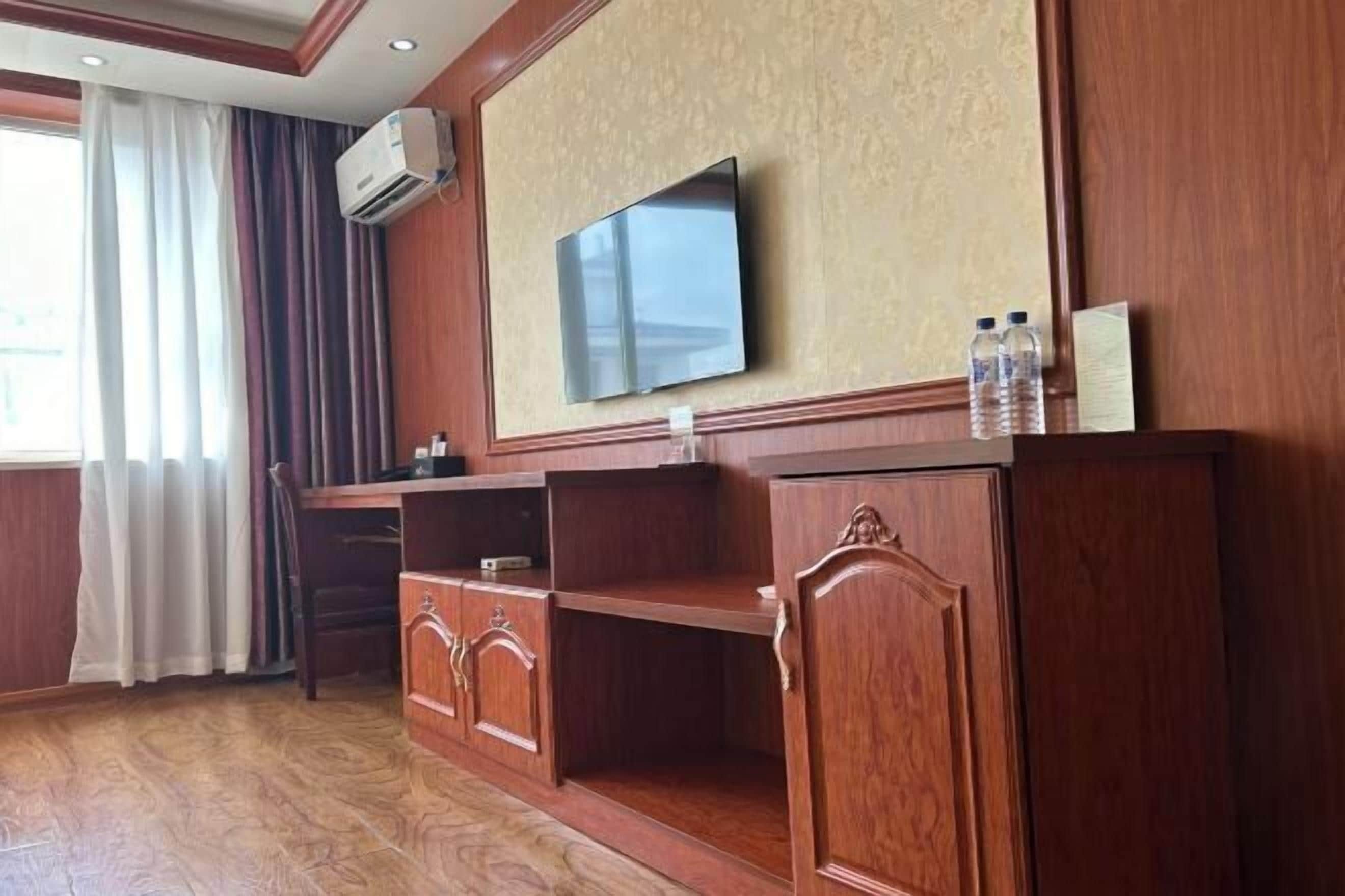 Una habitación con televisor montado en la pared, muebles de madera y una ventana con cortinas.
