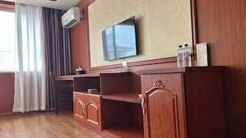 Una habitación con televisor montado en la pared, muebles de madera y una ventana con cortinas.
