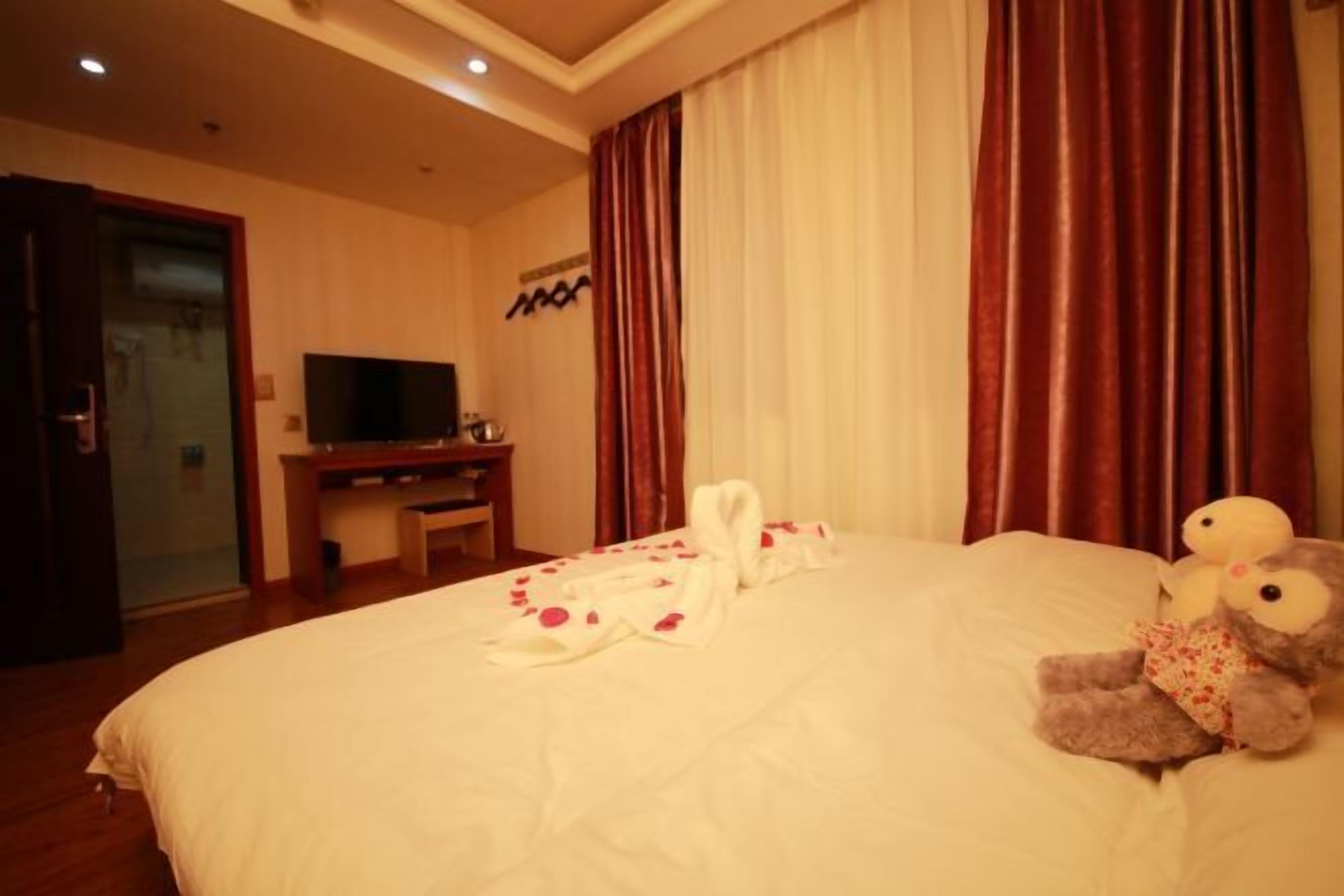 A hotel room with a large bed, a television on a stand, and a plush toy on the bed.