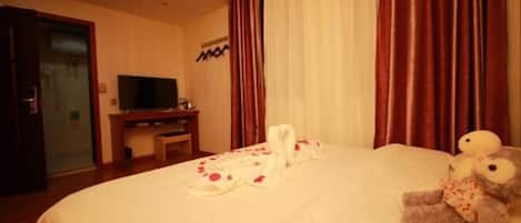 A hotel room with a large bed, a television on a stand, and a plush toy on the bed.