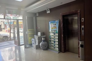 Egy szállodai előtér, amelyben recepció, lift és üvegajtós bejárat található.