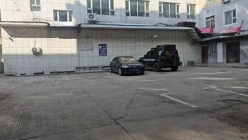 A parking area with a car and a van, a building with tiled walls, and a sign indicating parking availability.