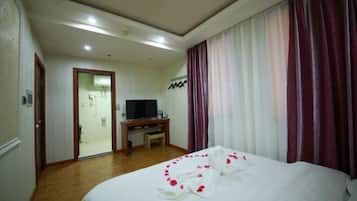 Habitación de hotel con cama, televisor, escritorio y baño visible a través de una puerta abierta.