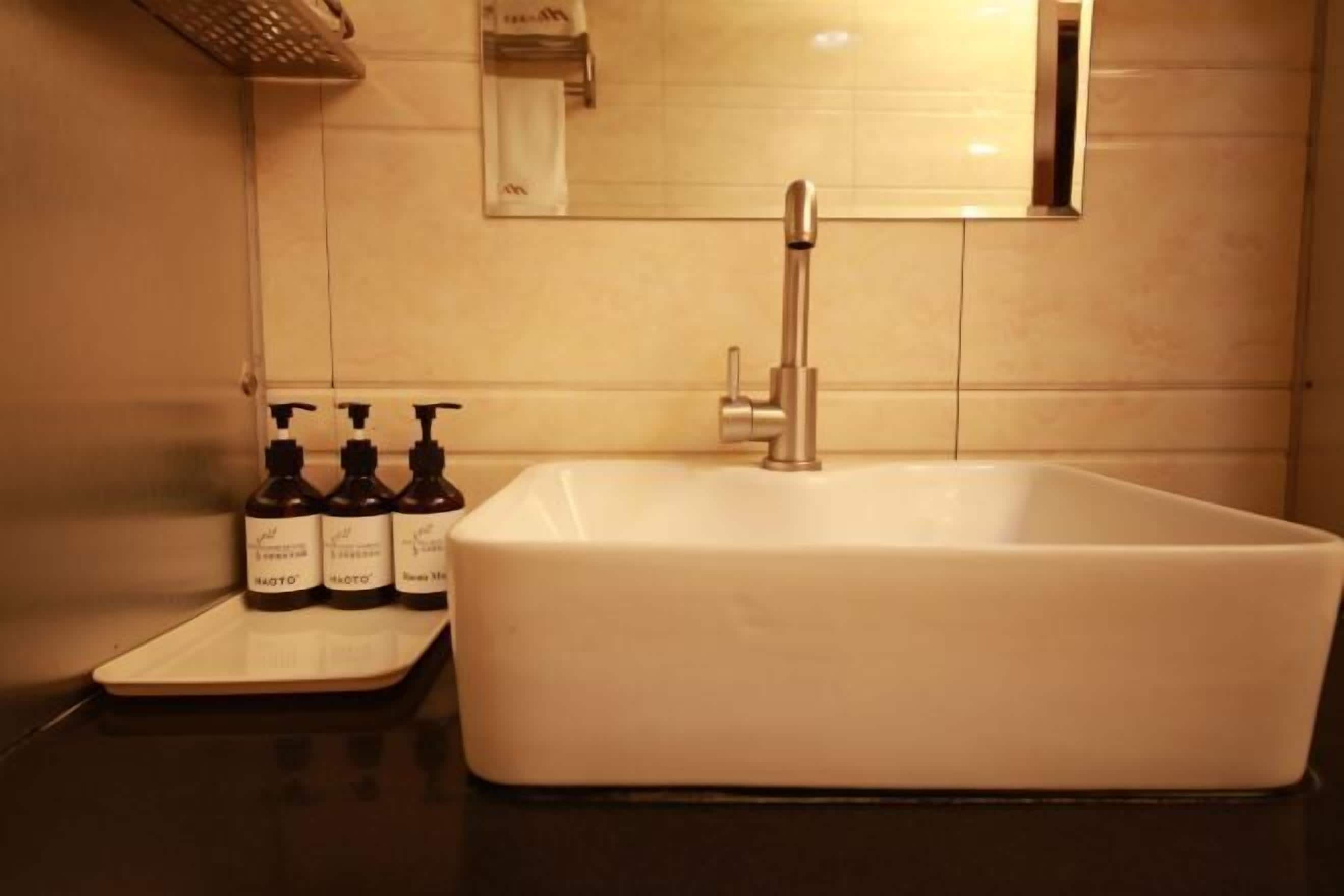A bathroom with a white sink, a mirror, and three bottles of hand soap on a tray.