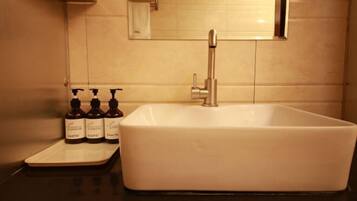 A bathroom with a white sink, a mirror, and three bottles of hand soap on a tray.