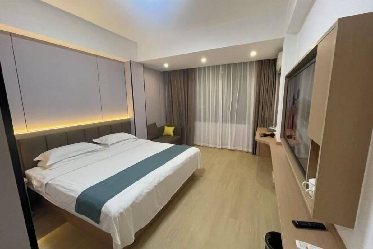 A hotel room with a large bed, a desk with a computer, and a window with curtains.