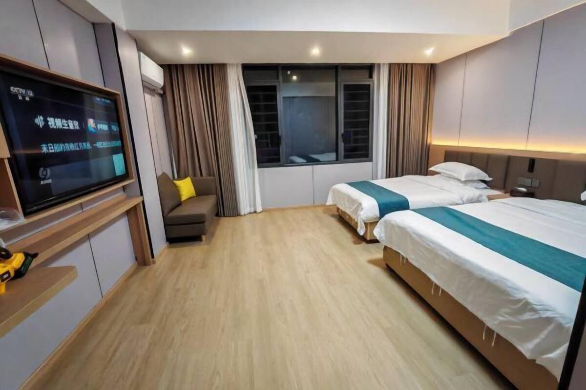 A hotel room with a TV, two beds, a sofa, and a window with curtains.