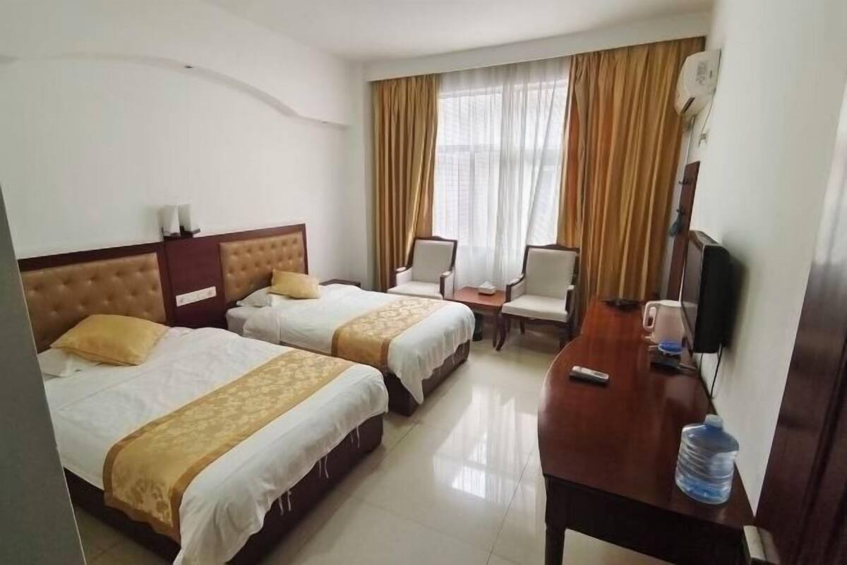 A hotel room with two beds, a desk, a chair, a television, and a window with curtains.
