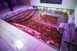 A stone-tiled pool with a wooden deck and a stone border.