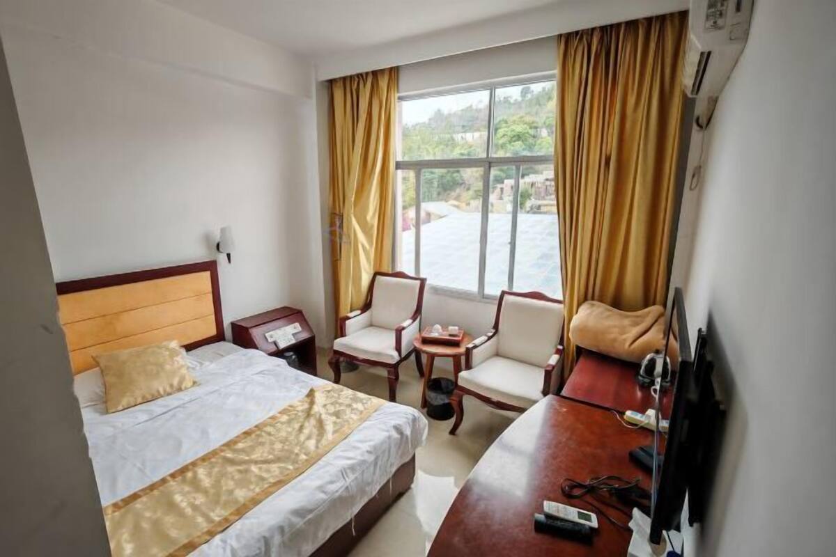 A hotel room with a bed, two armchairs, a desk, a TV, and a window with curtains.