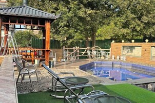 Un área de piscina con una estructura de madera, sillas de descanso y un pequeño puente.