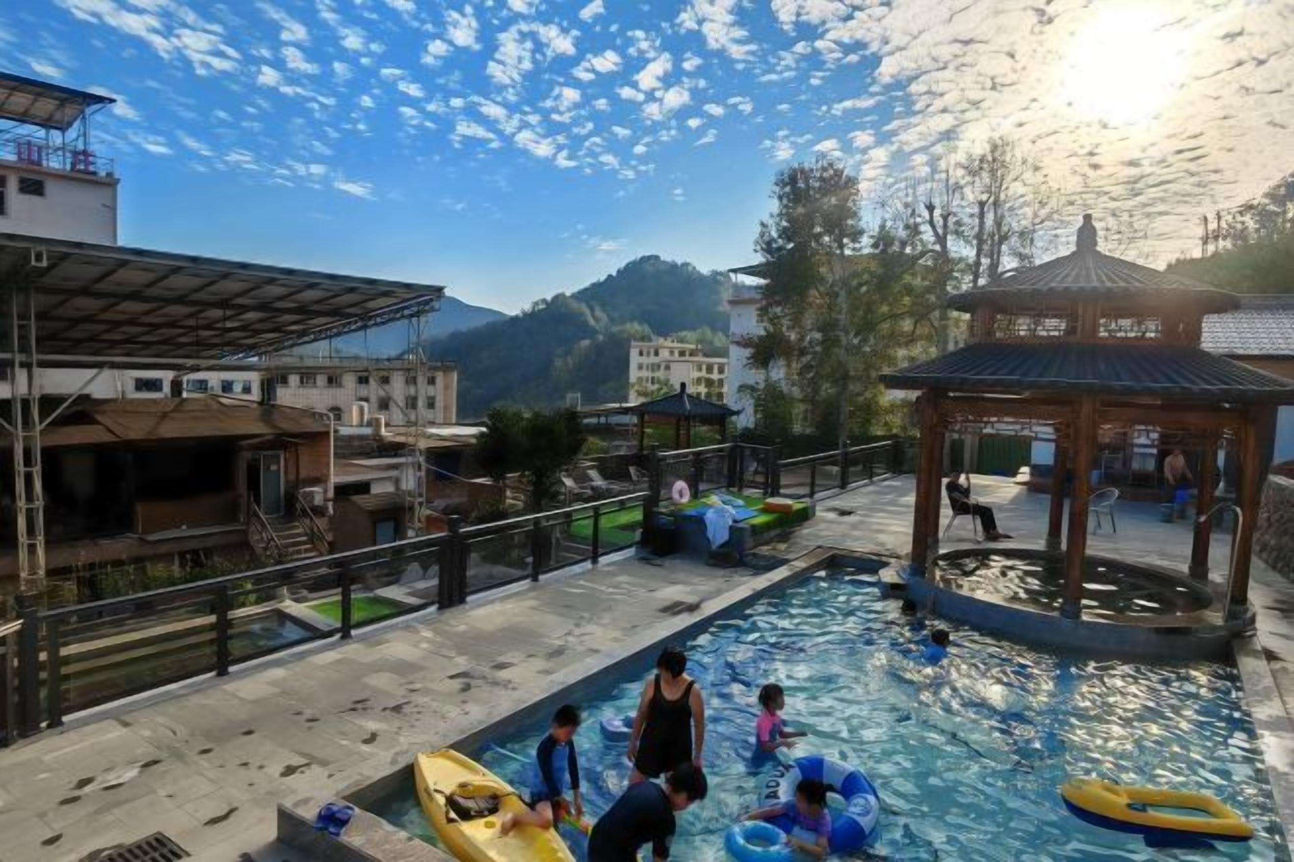 Un área de piscina con un quiosco, un bote pequeño y gente practicando actividades acuáticas.