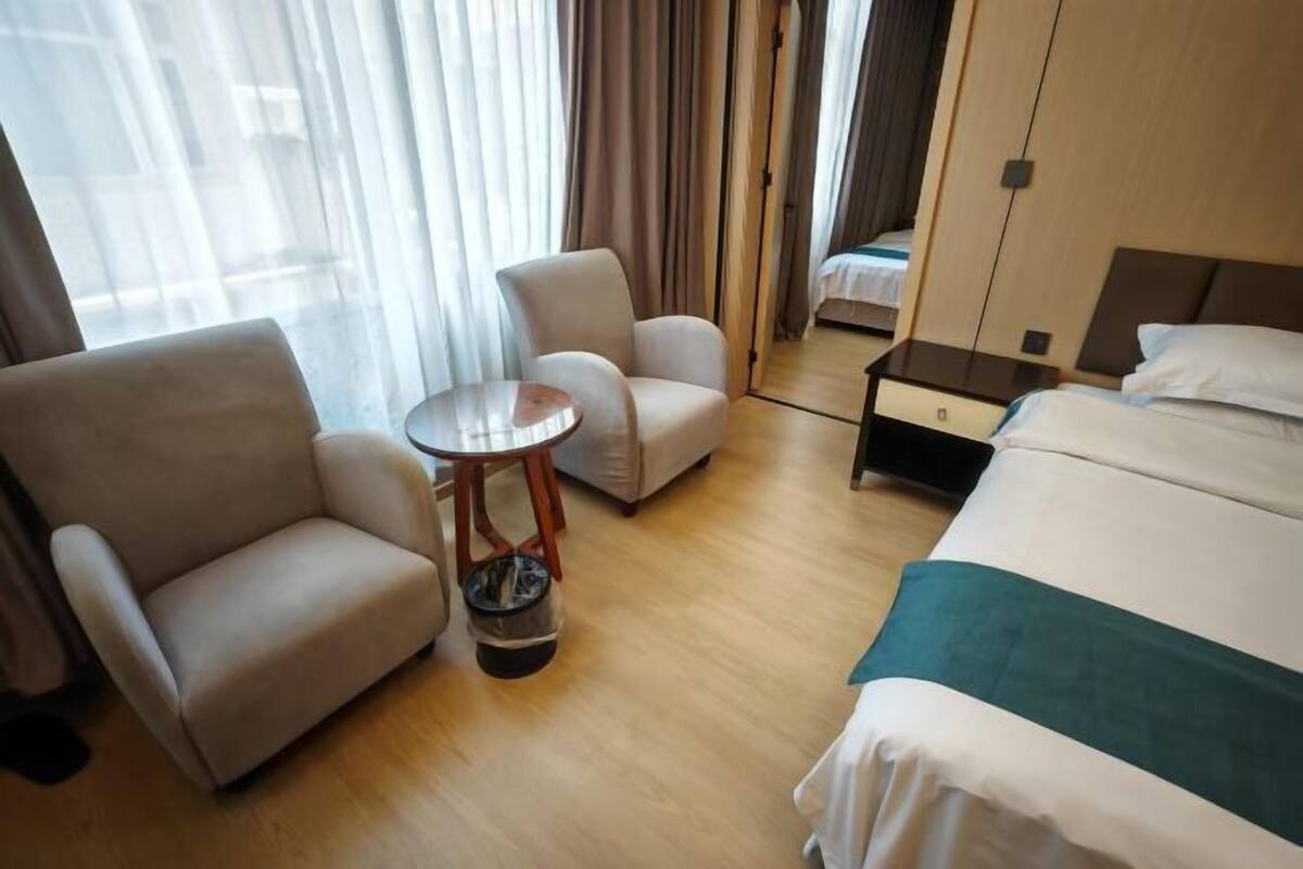 A hotel room with a bed, two armchairs, a small table, and a window with curtains.