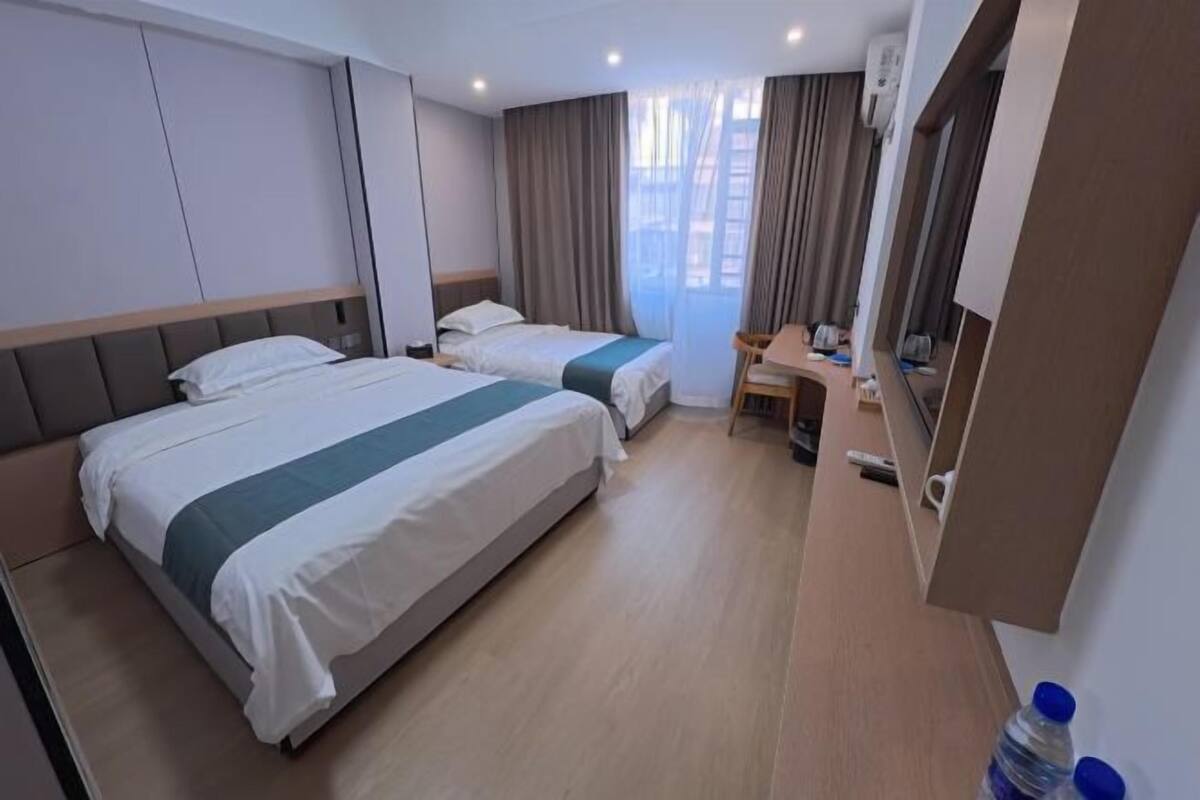 A hotel room with two beds, a desk, a chair, and a large window with curtains.