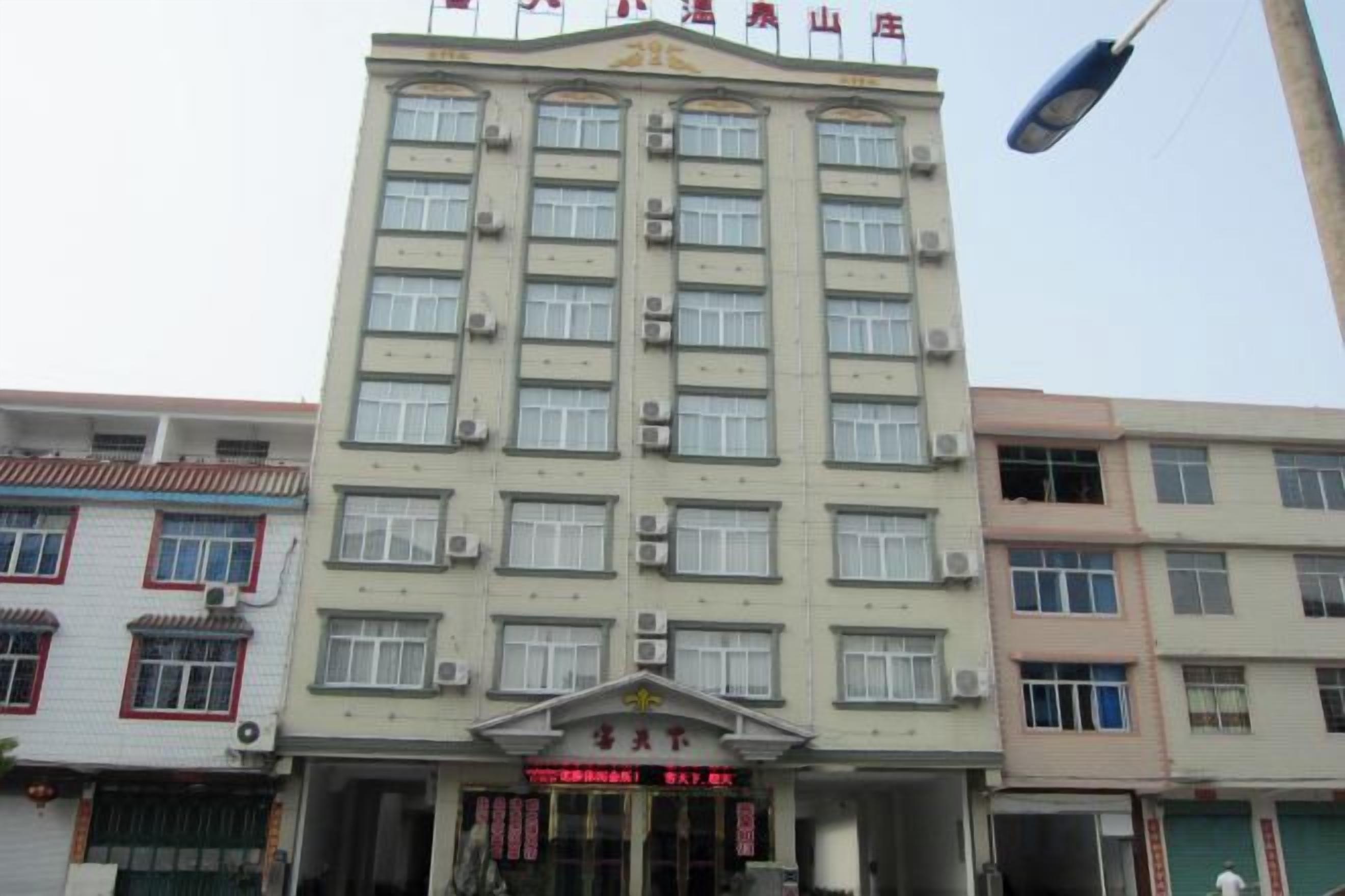 A multi-story hotel with a central entrance, air conditioning units, and a signboard.