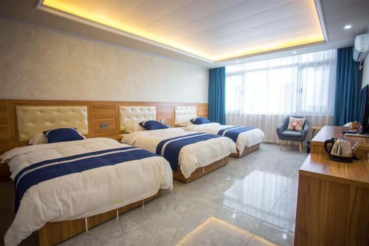 A hotel room with three beds, a wooden desk, a chair, and a window with curtains.