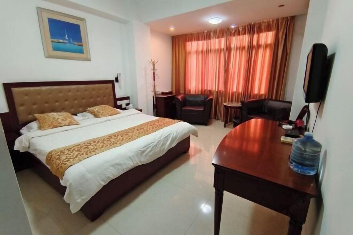 Habitación de hotel con una cama grande, un escritorio, una silla, una botella de agua y un cuadro en la pared.