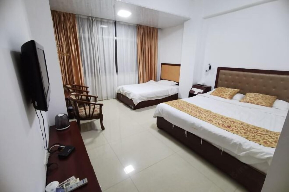 Habitación de hotel con dos camas, un escritorio con silla, televisión y mesita de noche.