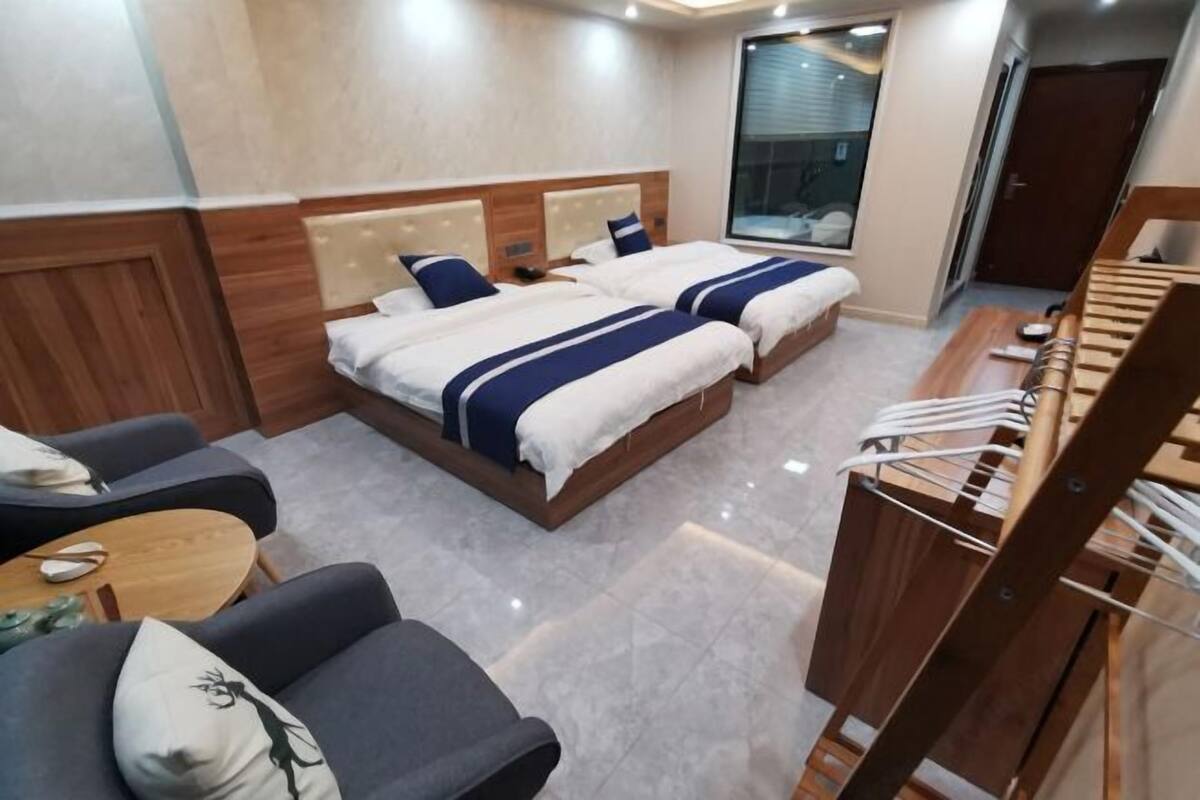 A hotel room with two beds, a desk, a chair, and a wardrobe.