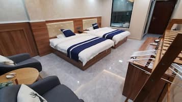 Habitación de hotel con dos camas, un sofá, una mesita y una silla de madera.