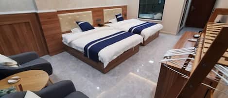 A hotel room with two beds, a sofa, a small table, and a wooden chair.