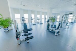 Un gimnasio con equipo de ejercicio, ventanas amplias y plantas en macetas.