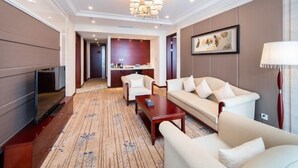 Habitación de hotel con sofá, sillón, mesa de centro, televisor y zona de comedor con sillas y mesa.