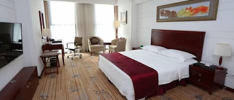 A hotel room with a large bed, a desk with a chair, a TV, and a painting on the wall.