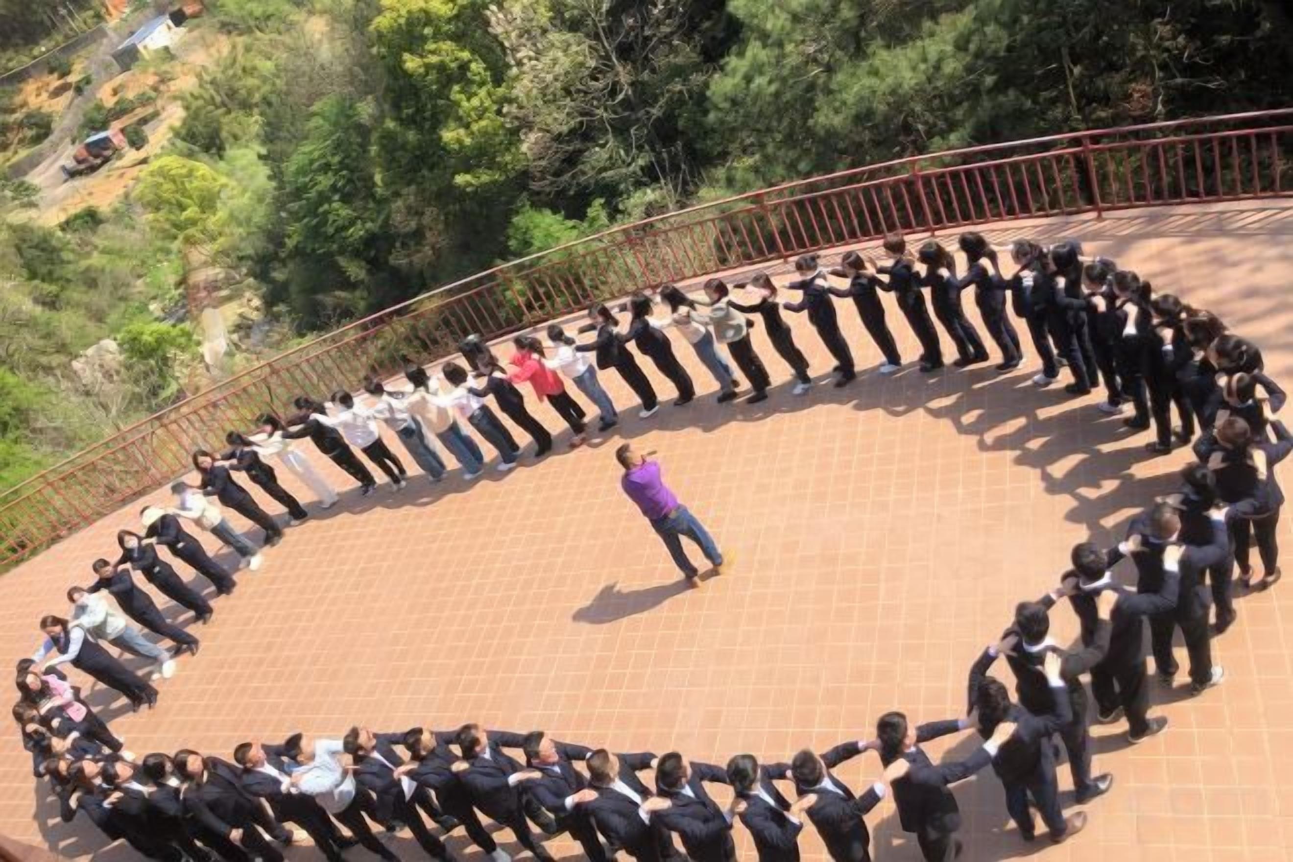 Un grupo de personas de pie en una formación circular sobre una superficie pavimentada, con barandilla alrededor.