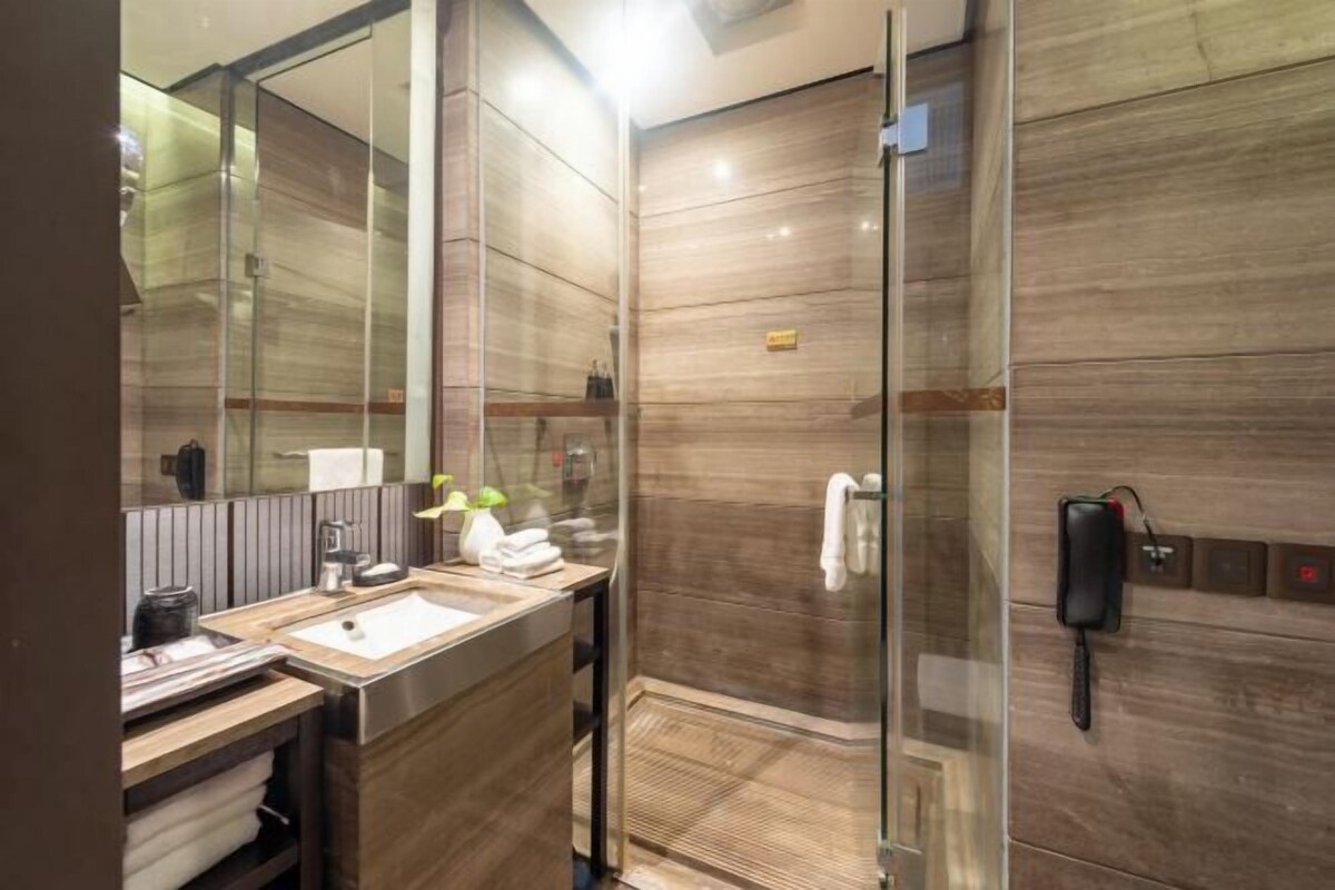 A modern bathroom with a glass shower enclosure, a sink with a mirror, and a telephone mounted on the wall.