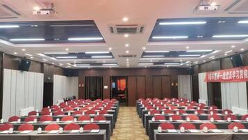 A conference room with rows of tables and chairs, equipped with ceiling lights and a projector.