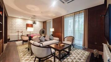 A modern hotel room with a sofa set, a coffee table, a fireplace, and a large window with curtains.