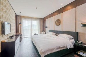 A hotel room with a large bed, a desk with a chair, a TV mounted on the wall, and a window with curtains. - Nanchang Qinyuan Villa (Nanchang)