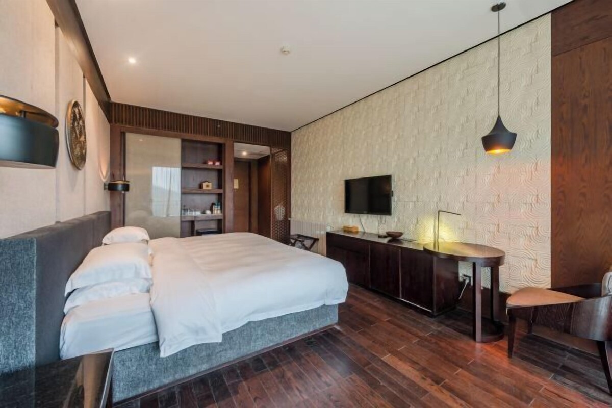 A modern hotel room with a large bed, a TV, a desk with a lamp, and a wooden cabinet.