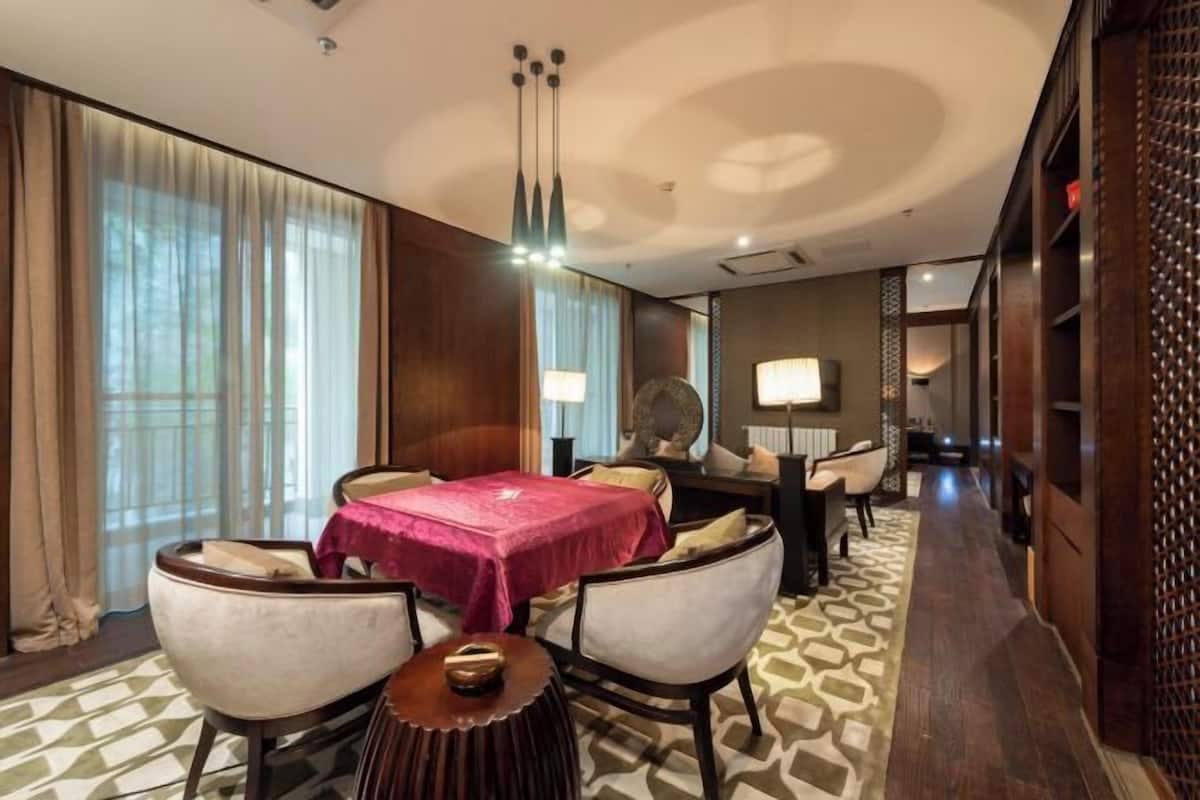 Une chambre d’hôtel avec un coin repas, une table ronde recouverte d’une nappe rouge et un tapis à motifs.