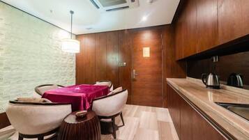 A modern kitchen with wooden cabinets, a marble countertop, and a dining area with a table and chairs.