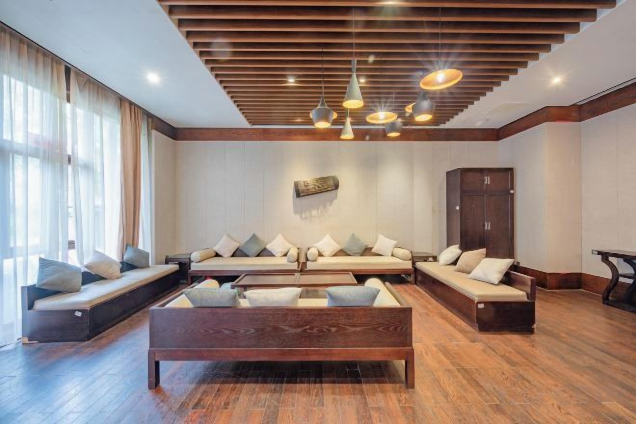 A spacious living area with a large sofa set, a wooden coffee table, and a high ceiling with wooden beams and pendant lighting.