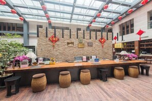 Un área de recepción con mostrador de madera, diversas opciones de asiento y una pared de piedra con adornos rojos.